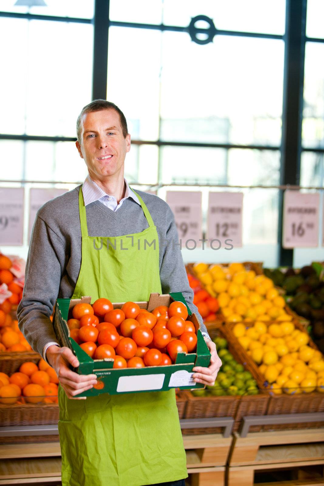 A friendly grocery store owner with a box of ripe tomatoes