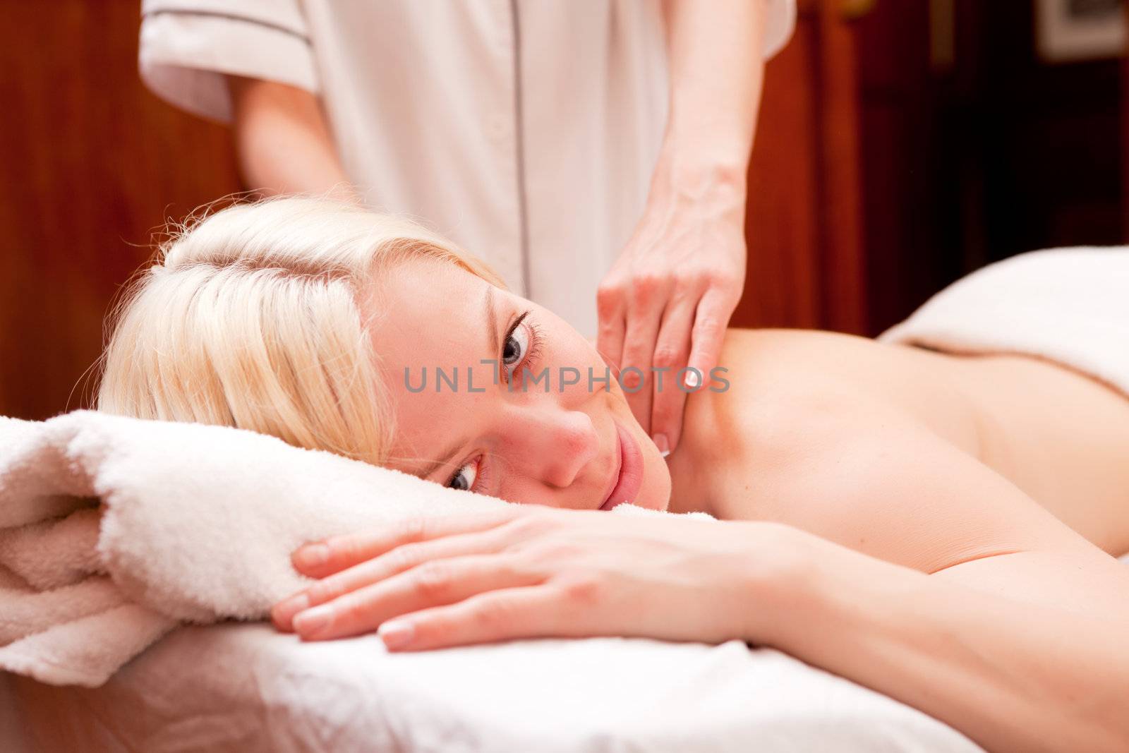 A happy blond woman looking at the camera receiving a shoulder massage