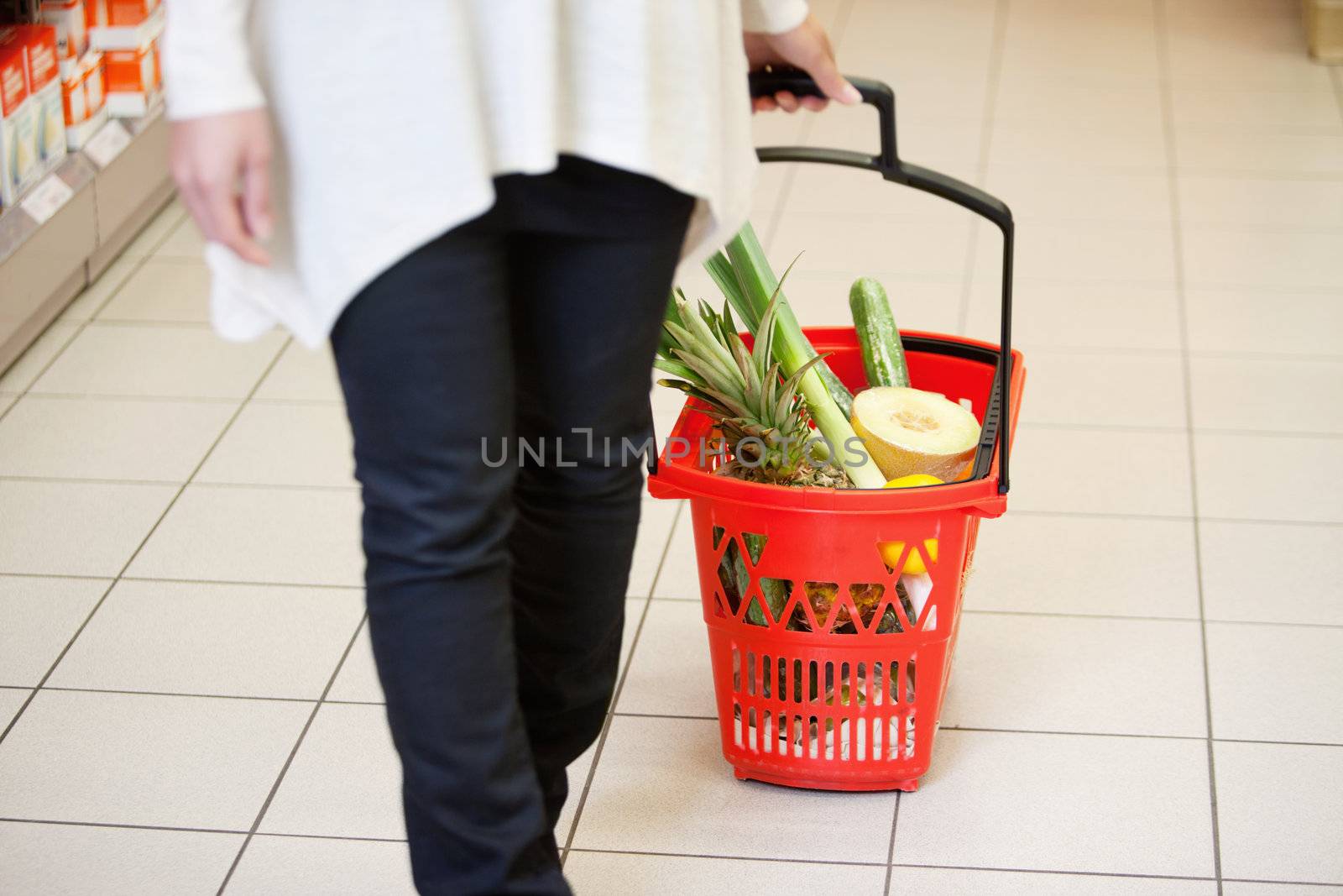 Woman holding handle of red basket in shopping store