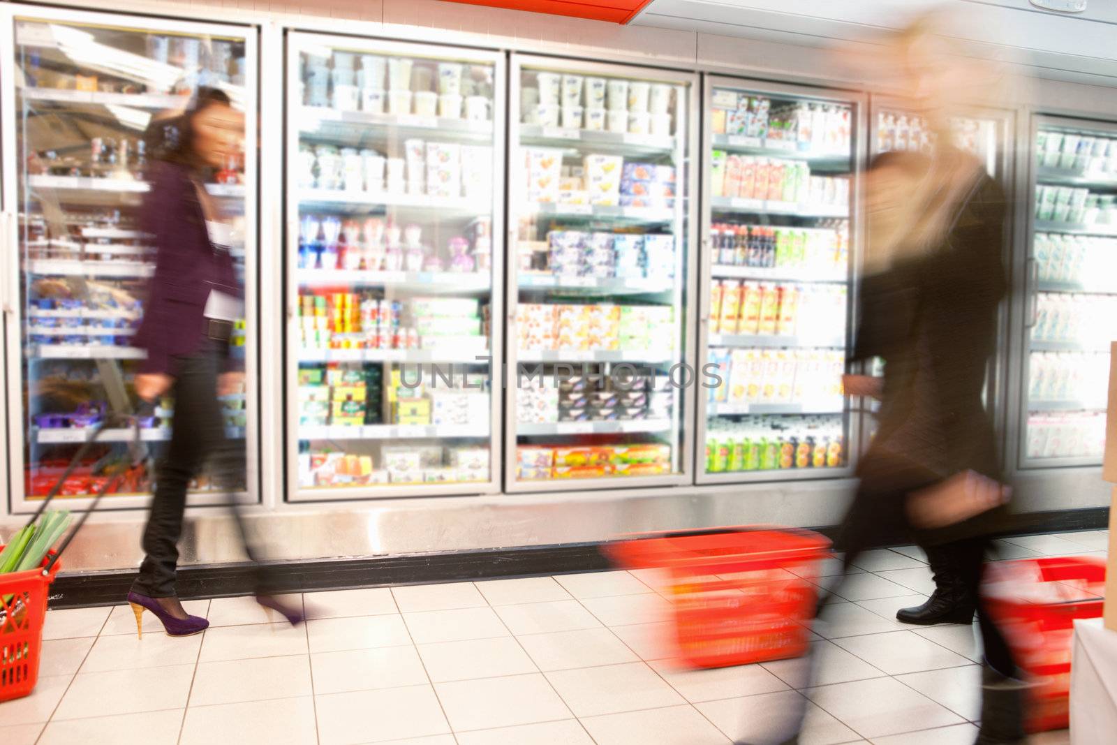 Blurred motion of people walking near refrigerator in shopping centre with baskets