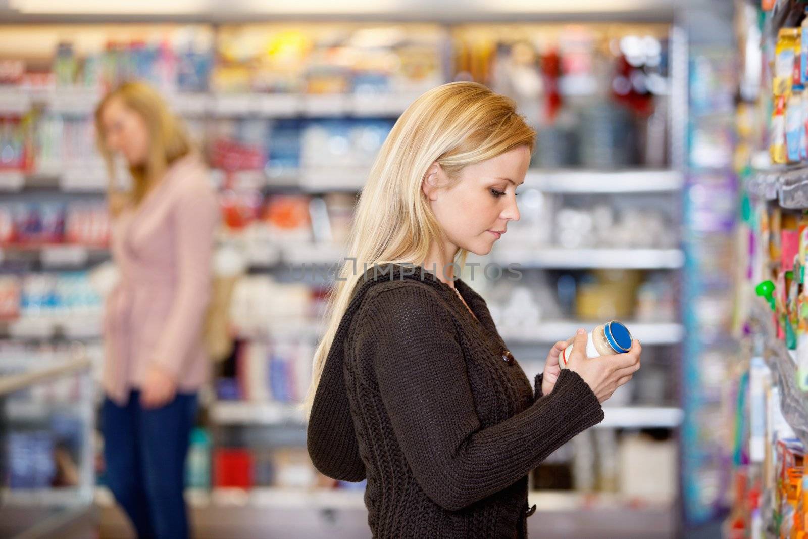 Young woman comparing products in the supermarket with people in the background