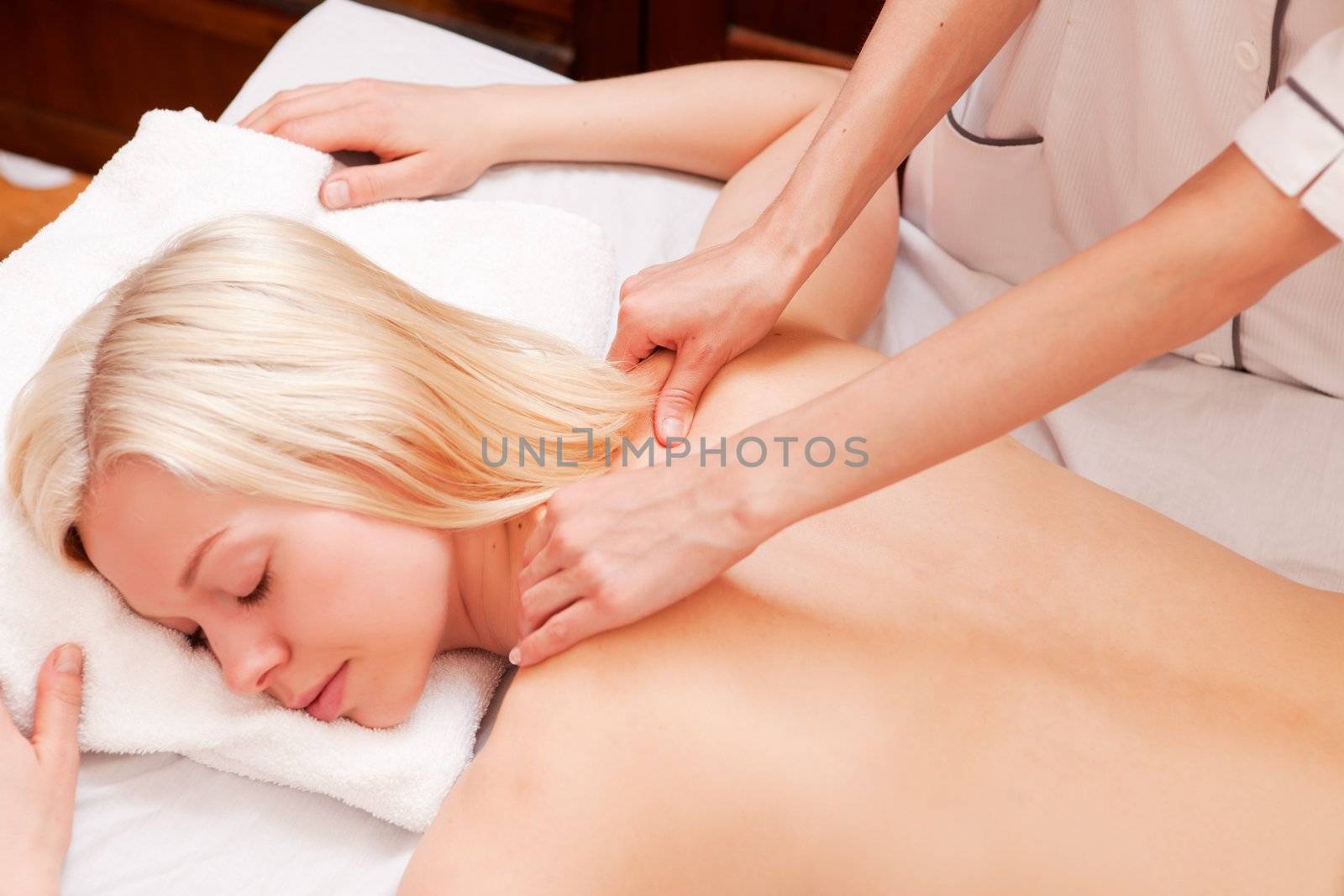 A pretty woman receiving a shoulder massage at a spa - shallow depth of field, focus on massage hands