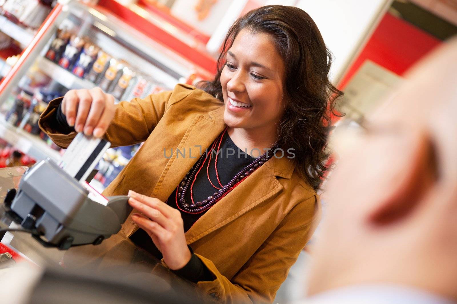 Shop assistant smiling while swiping credit card in supermarket with customer in the foreground