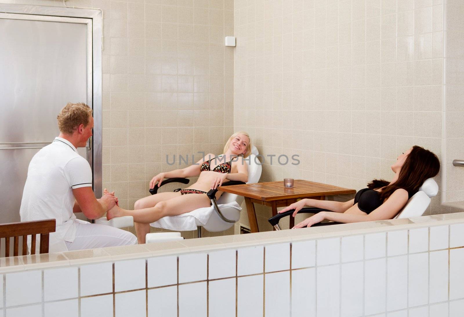 A woman receiving a foot massage with a friend in a spa