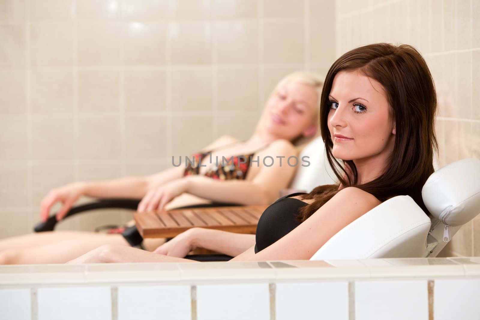 Two women relaxing in chairs beside an indoor pool