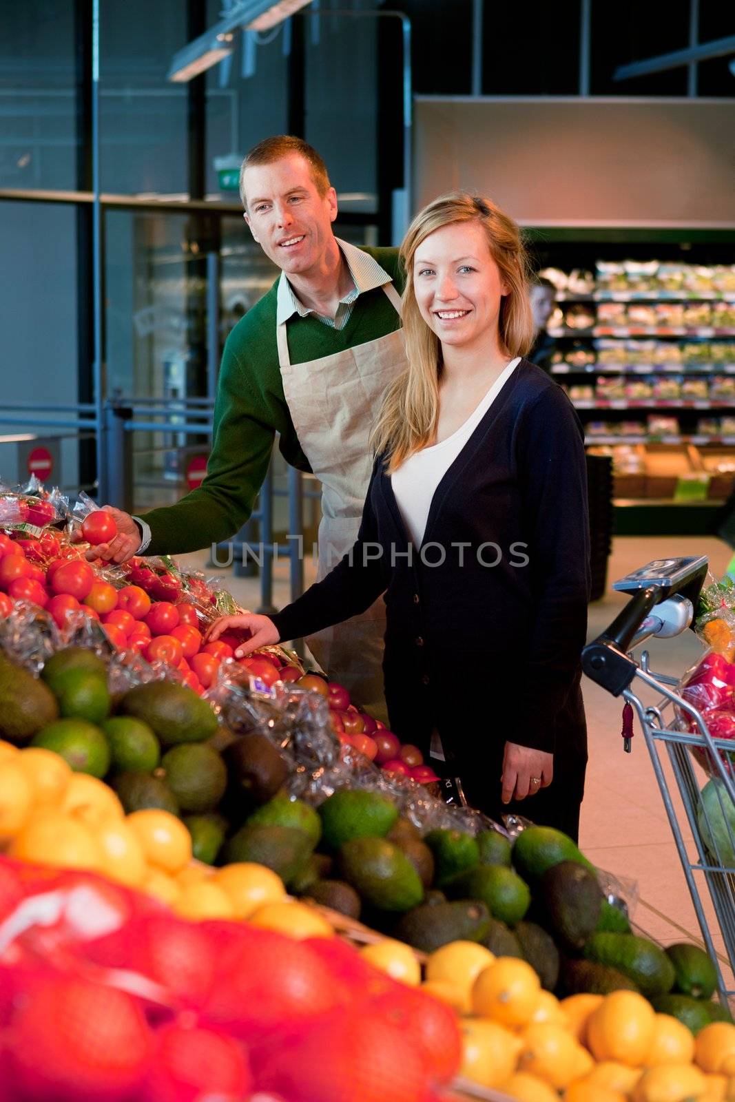 A woman buying fruit and vegetables at a supermarket, receiving help from a grocer