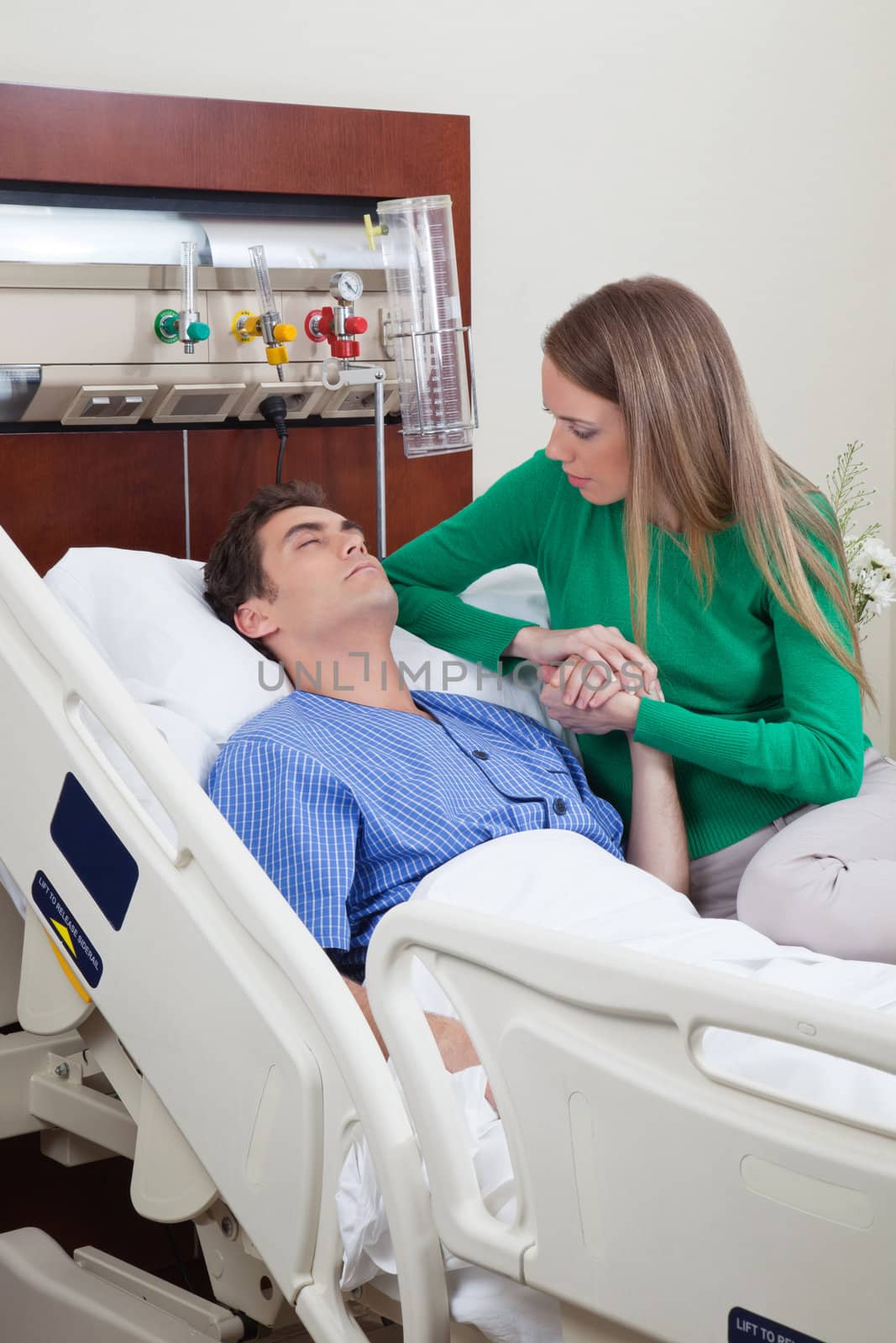 Man on a hospital bed with woman holding his hand with concern