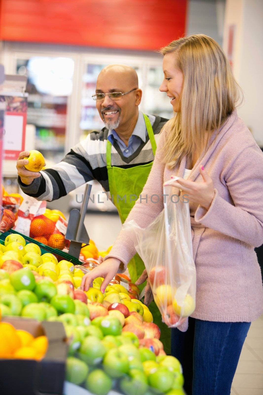 Happy young woman buying fruits with shop assistant in the background