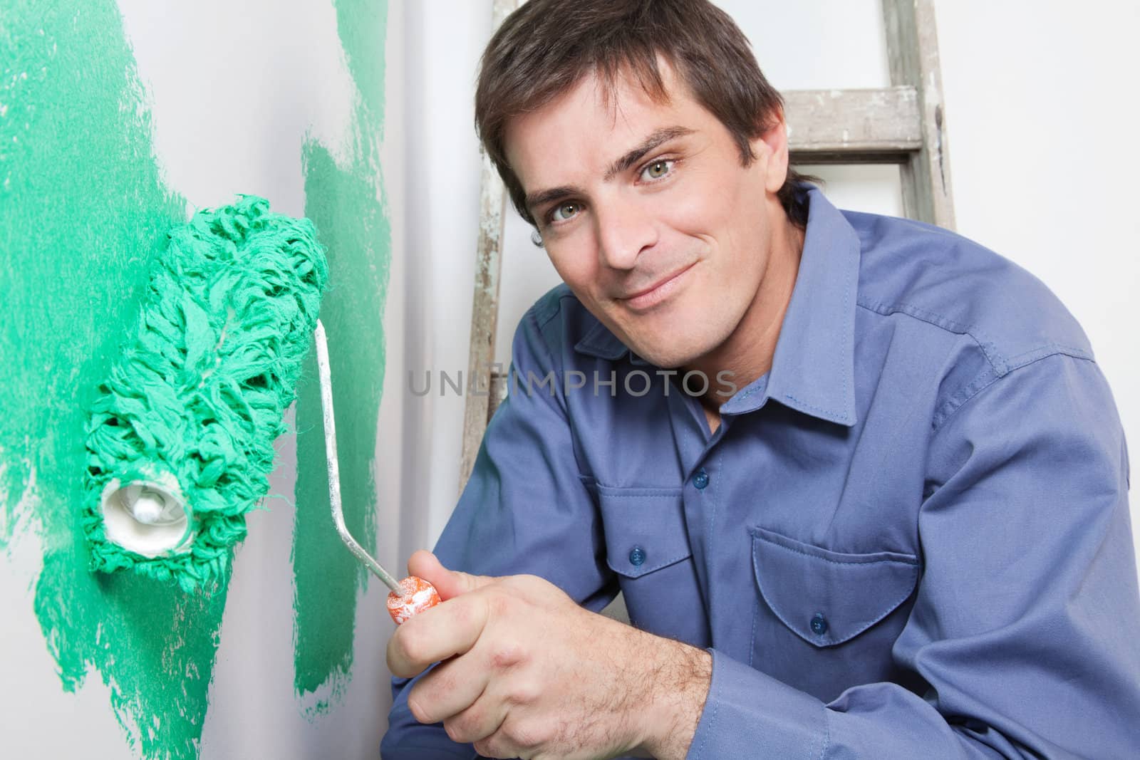 Portrait of happy mature man painting the wall with a roller