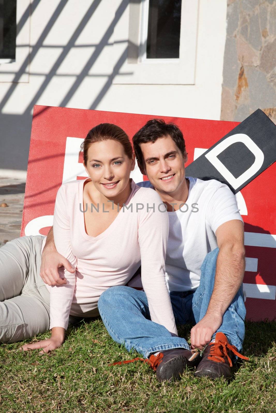 Portrait of happy young couple sitting in front of their new home