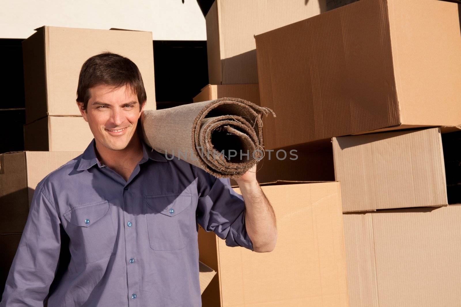 A moving an carrying a carpet with cardboard boxes in the background