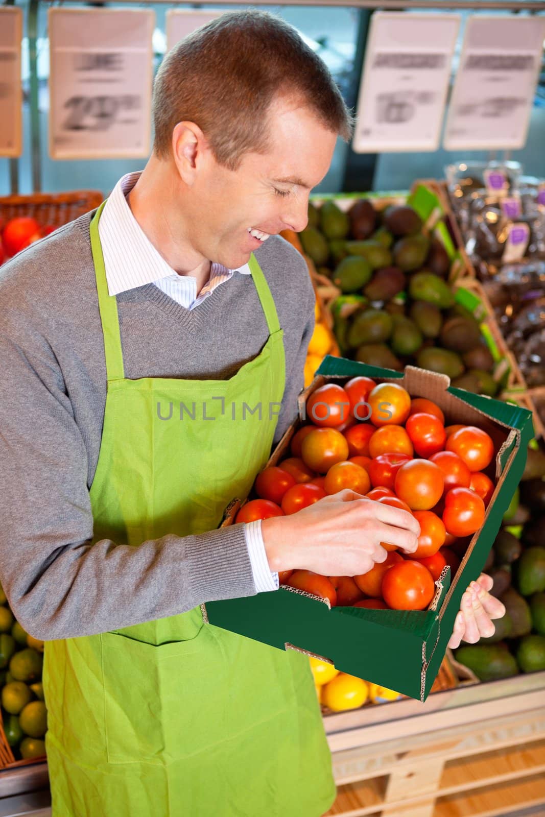 Happy market assistant holding box of tomatoes in the supermarket