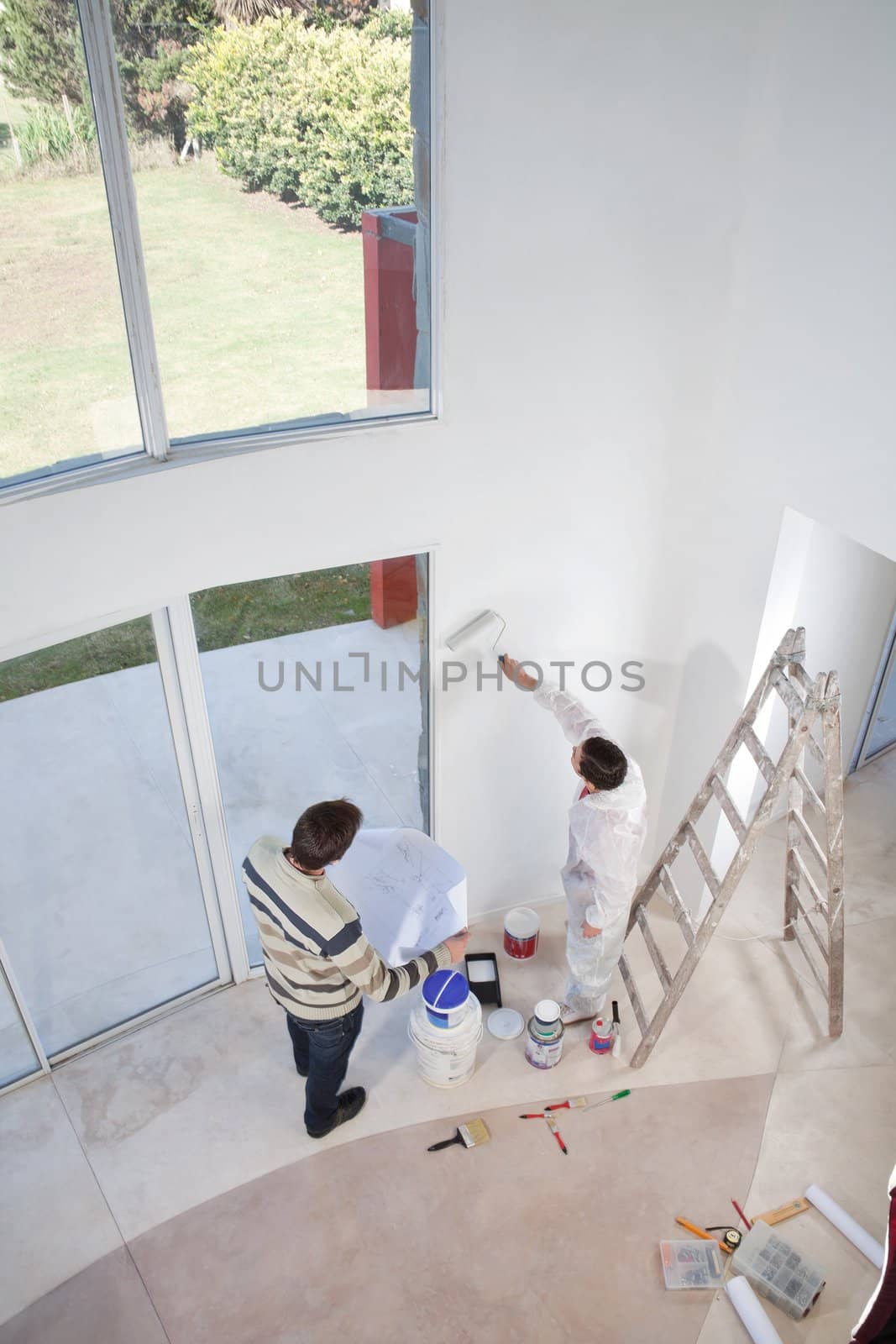 High angle view of man holding blueprint and workman painting the wall
