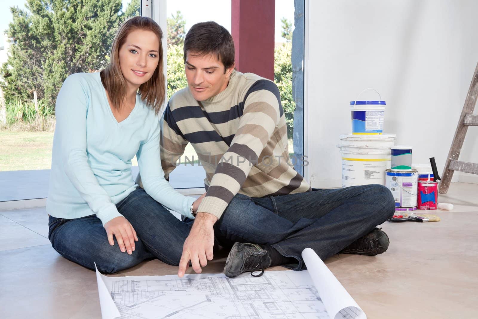 Mature couple sitting on the floor with blueprint of their new house