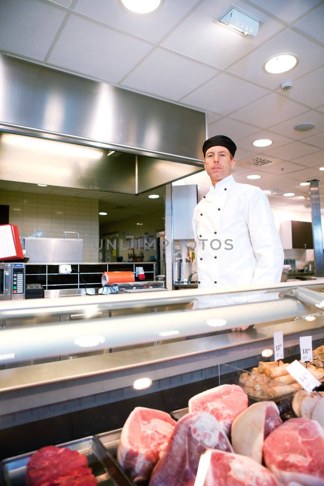 A serious satisfied butcher behind a fresh meat counter in a deli