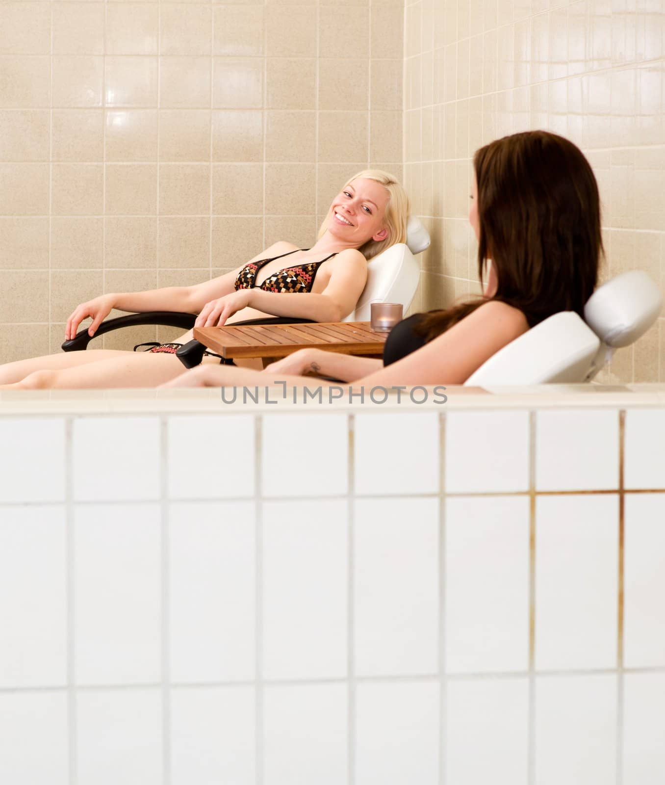 Two women relaxing and visiting beside an indoor pool