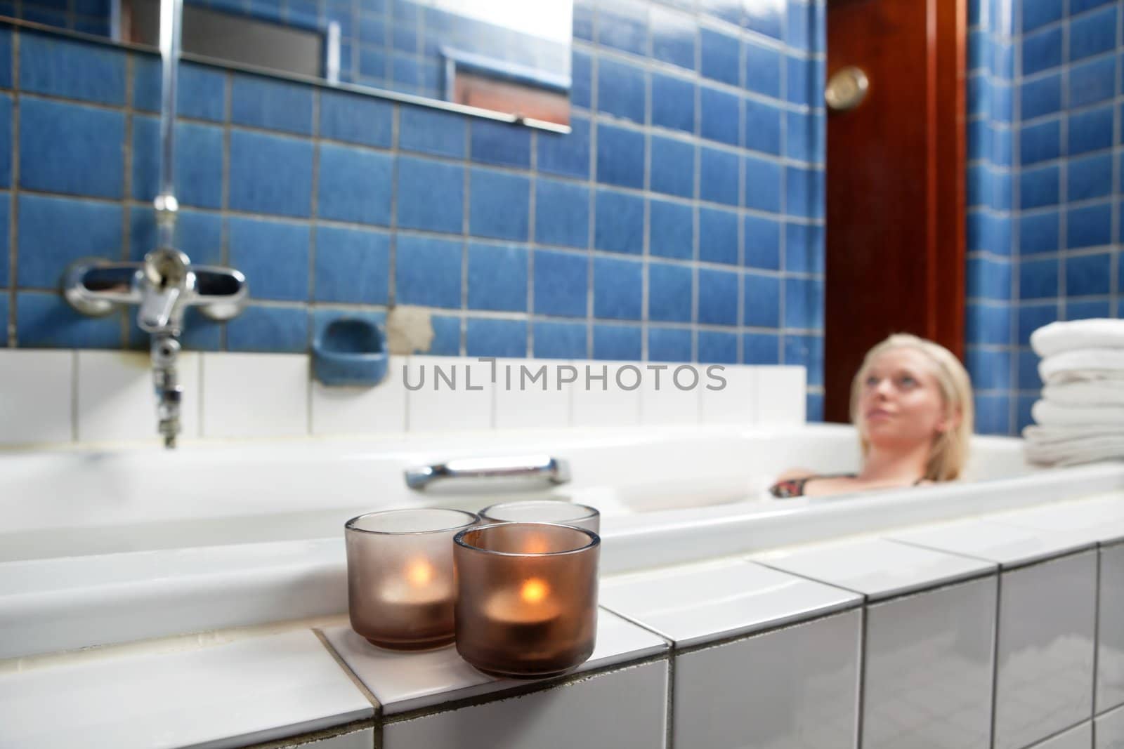 Beautiful young woman relaxing in bathtub with candles in foreground