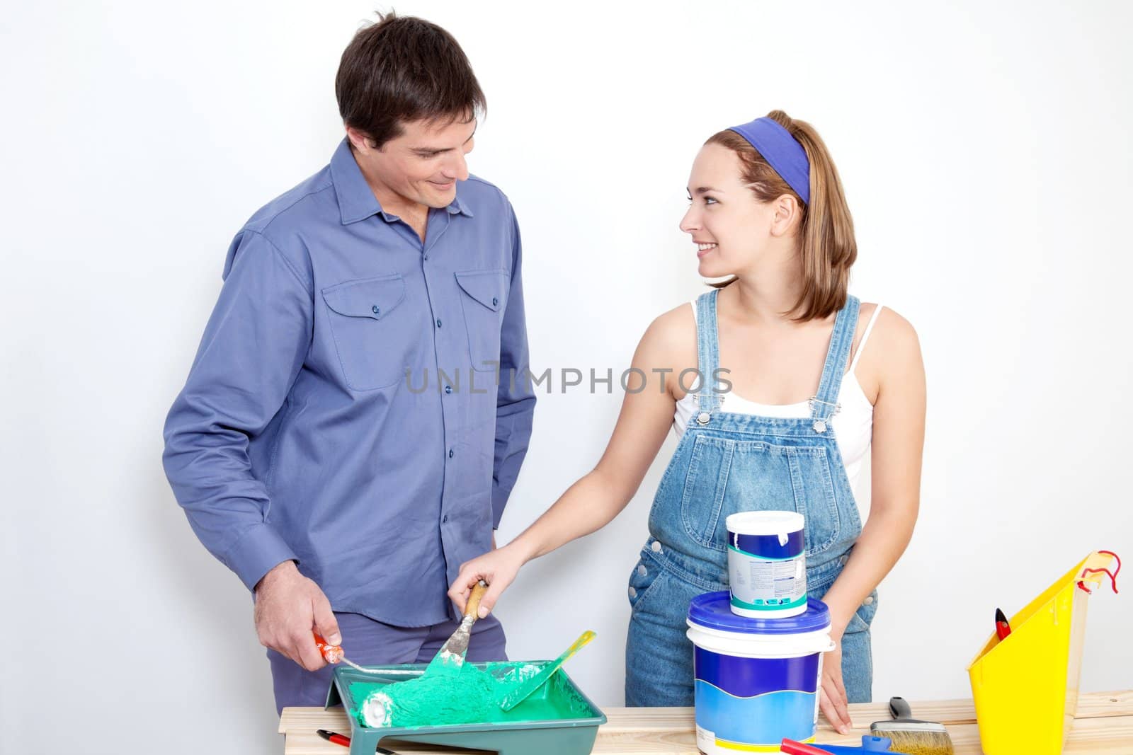 Happy mature couple with roller, paint and bucket on table at their new apartment