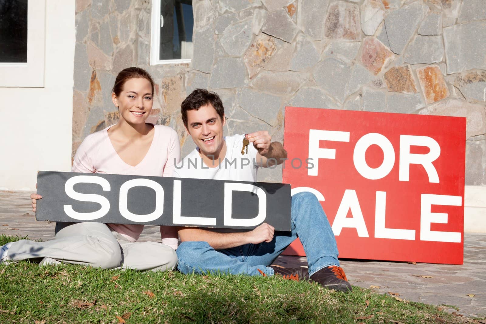 Happy young couple holding a sold placard in front of their new home