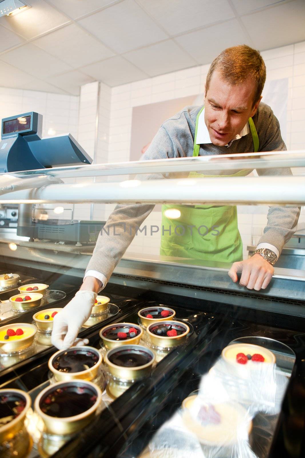 A man selling gourmet deserts from behind a glass counter