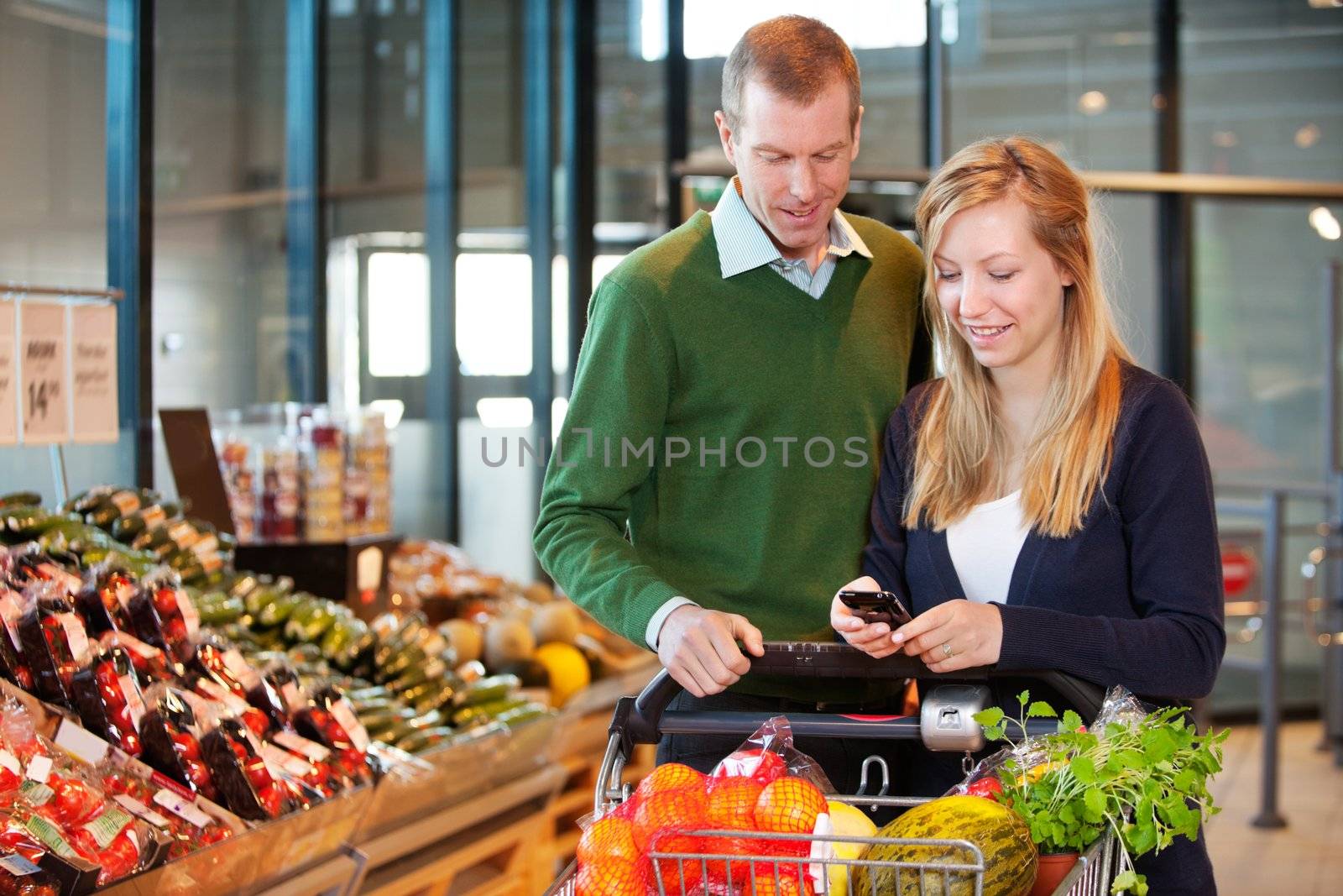 A happy couple buying groceries looking at grocery list on phone