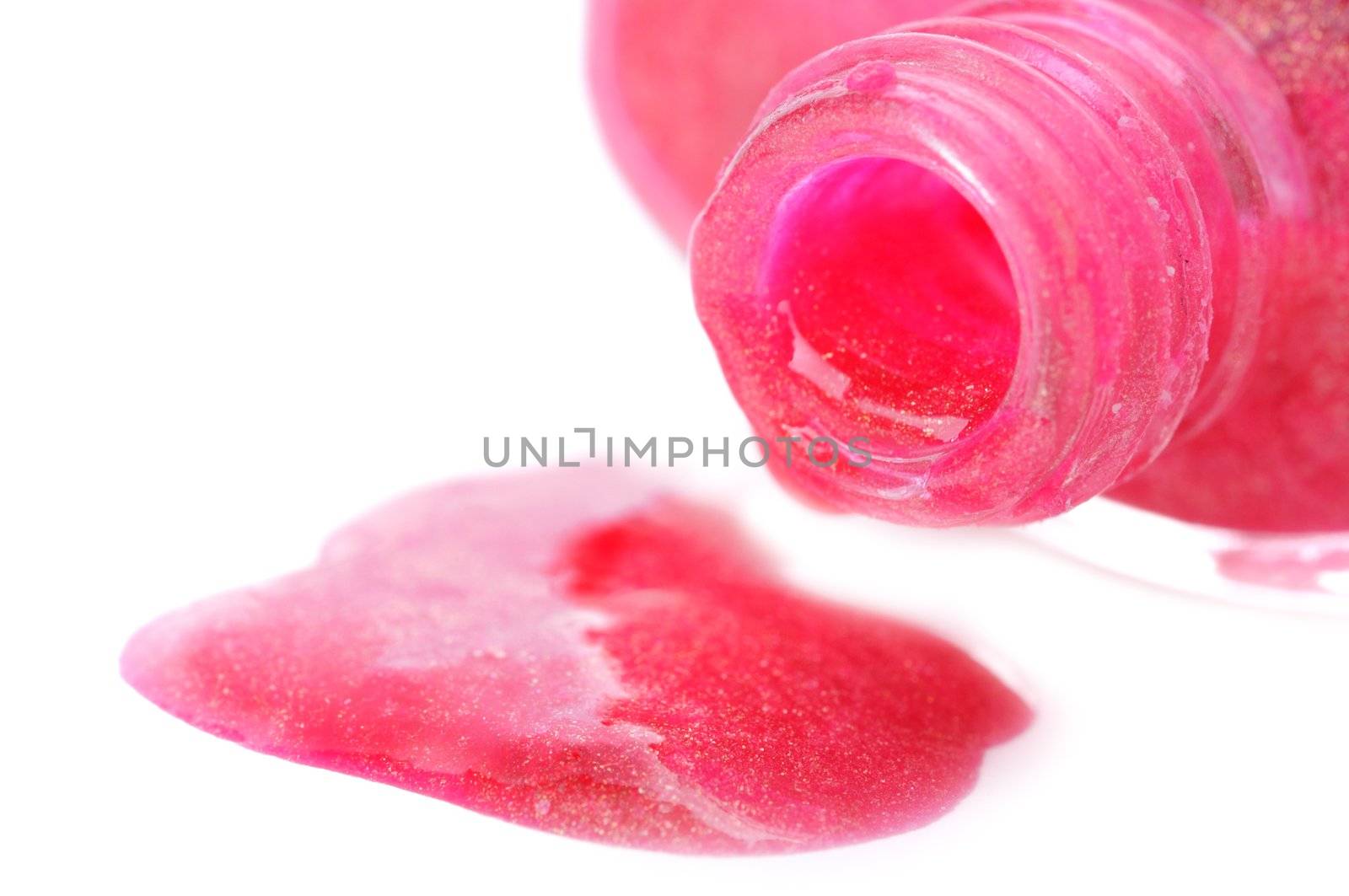 Close-up of open nail polish bottle and poured rose polish on white background. Shallow depth of fields. Focus on bottleneck.