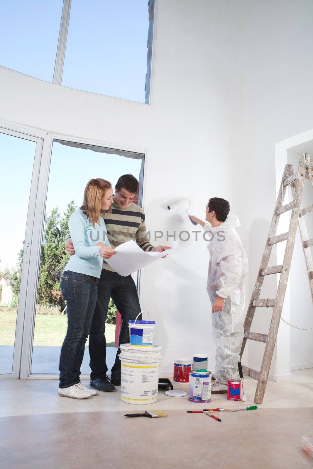 Young couple looking at blueprint while worker painting their house