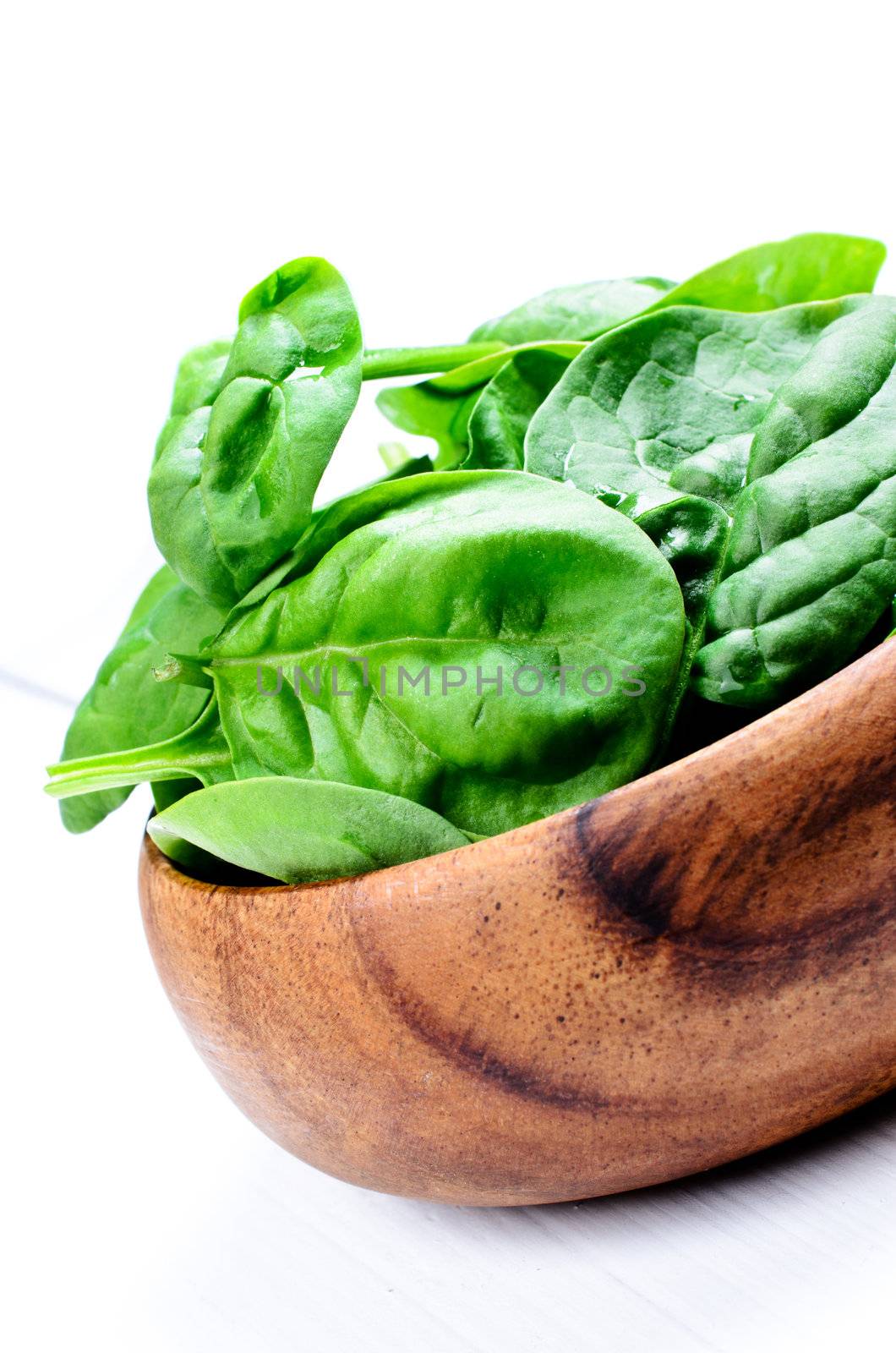 Wooden bowl of spinach on white table by Nanisimova