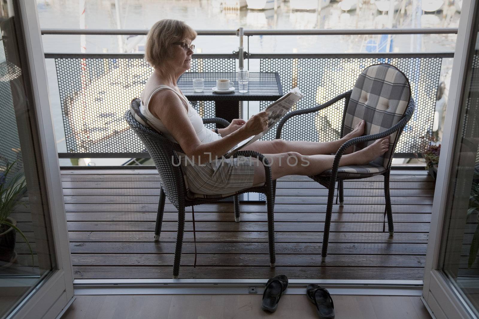 SENIOR SUMMER LIFE, NYBORG, DENMARK, AUGUST 20, 2012: Female senior enjoying her morning coffee and newspaper on the balcony of her waterfront flat. Temperature already 24 C in the shade.