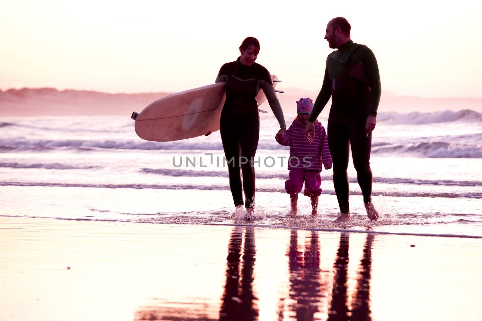 Female surfer and her familly walking in the beach at the sunset