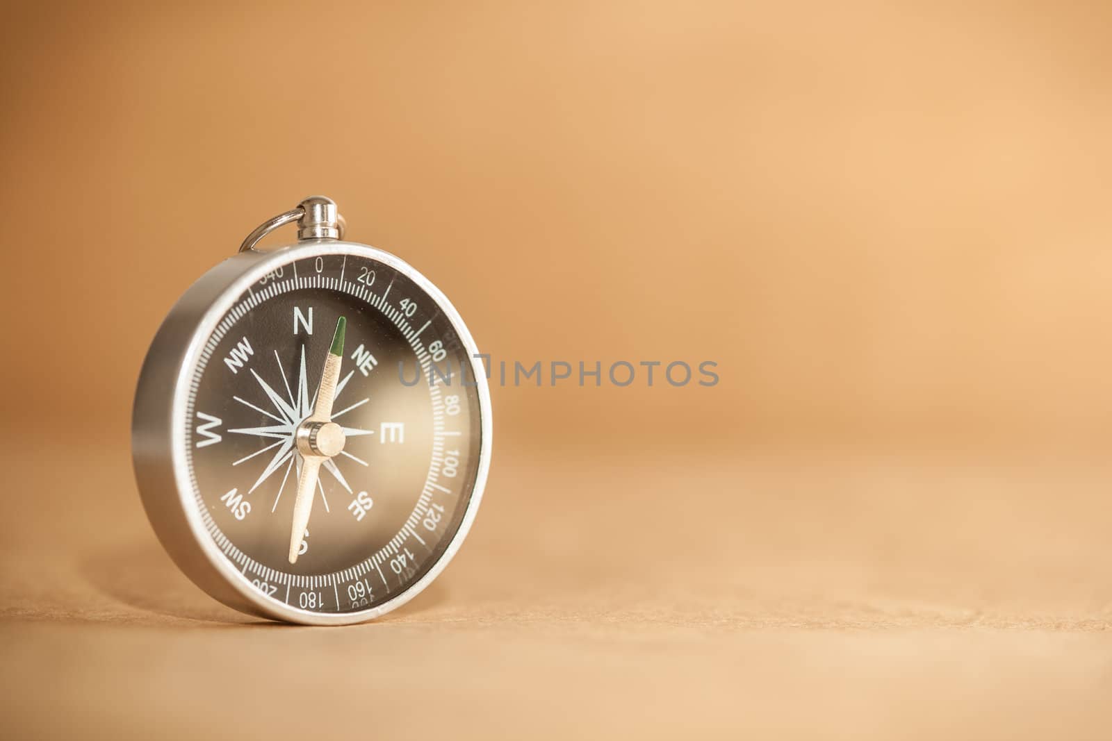A silver compass with black face pointing north on a brown paper background.