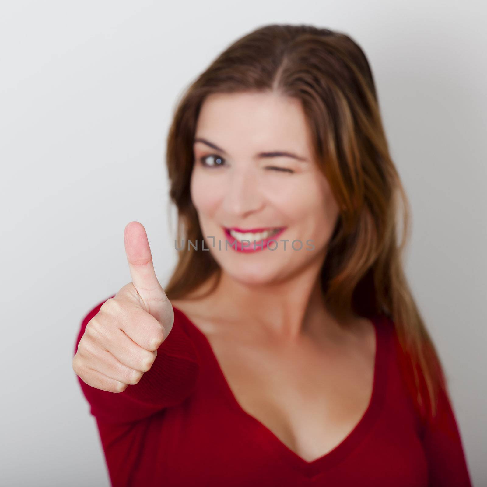 Beautiful and happy woman with thumbs up, against a gray wall