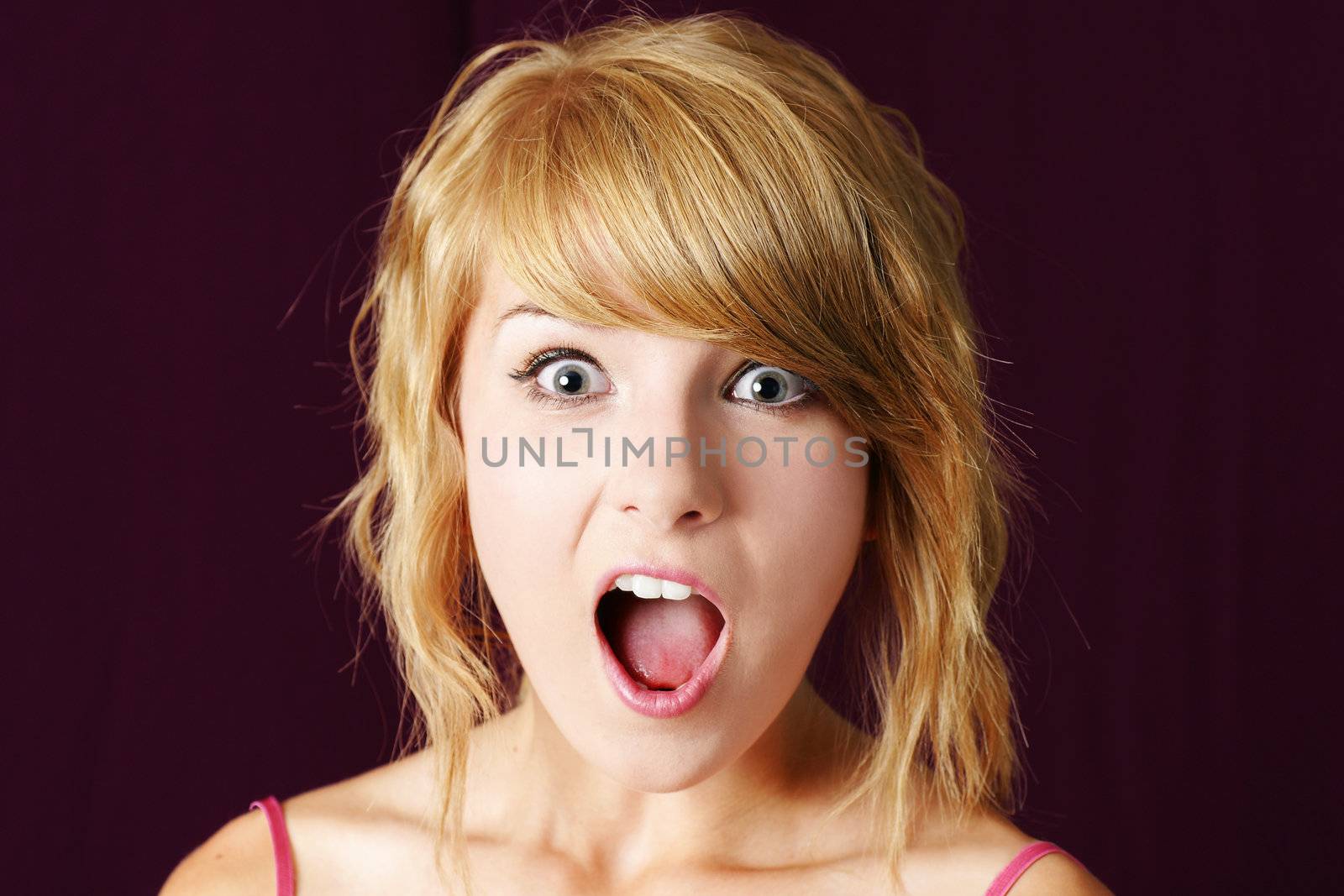 Very surprised or shocked young blond teenager girl making funny face, with eyes and mouth wide open, studio shot.