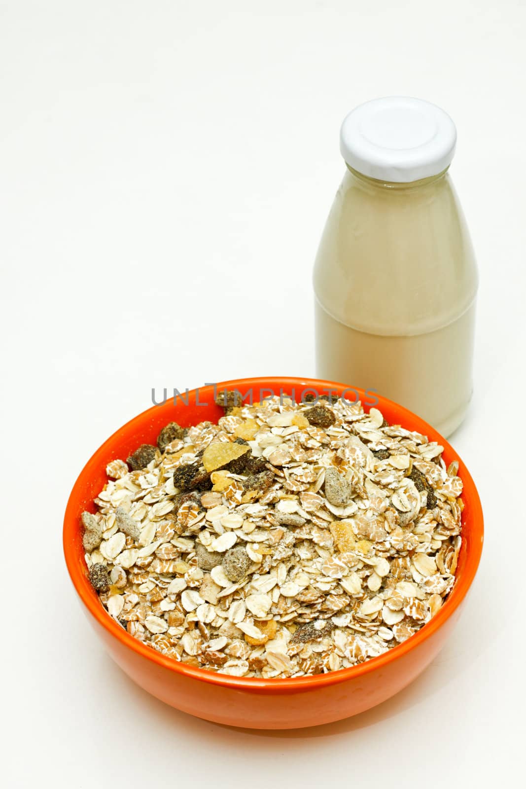 Orange bowl of cereal with a glass bottle of  milk.