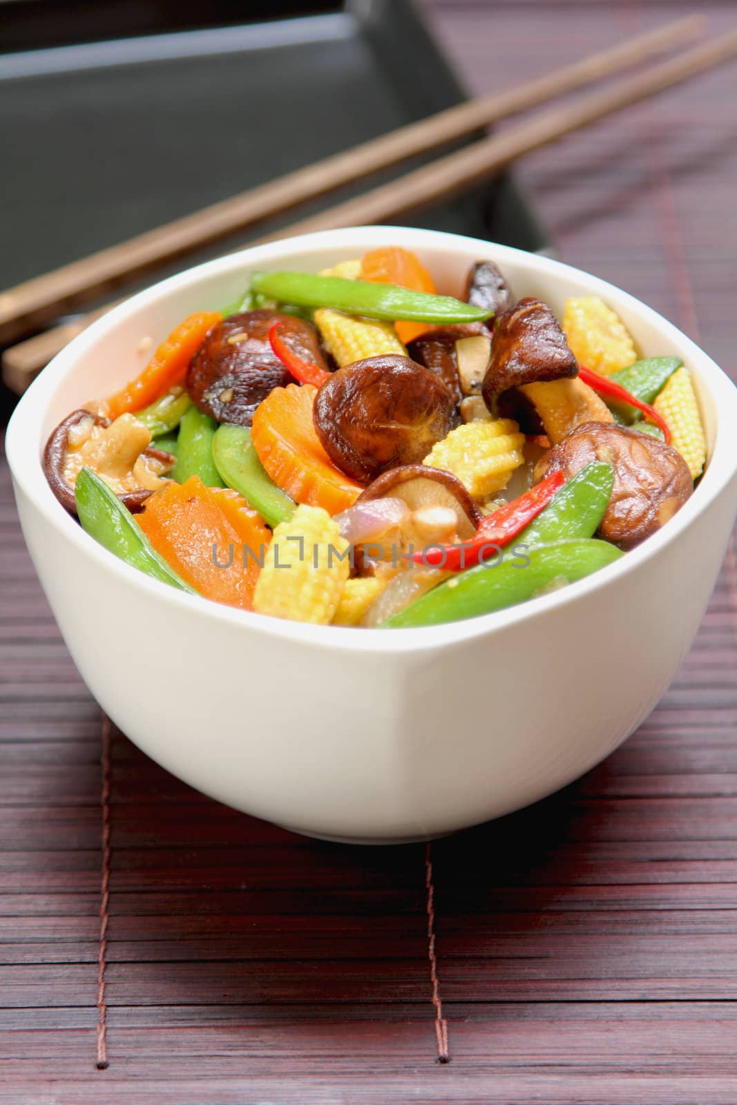 Stir fried vegetables with mushroom in white bowl by chopstick