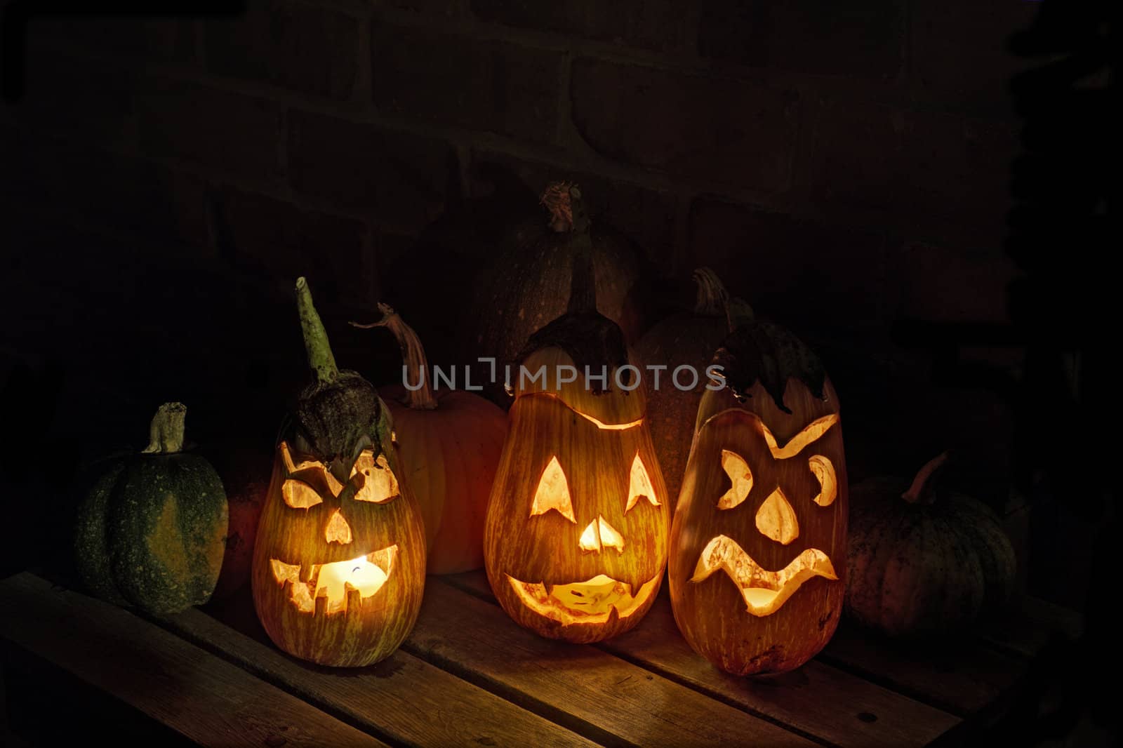 HDR image of carved eggplant jack o'lanterns with pumpkins and other squashes on a small table in teh dark form part of a display for the halloween holiday