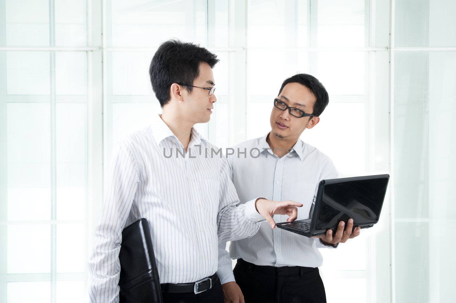 Two Asian young executives working on laptop, office building as background 