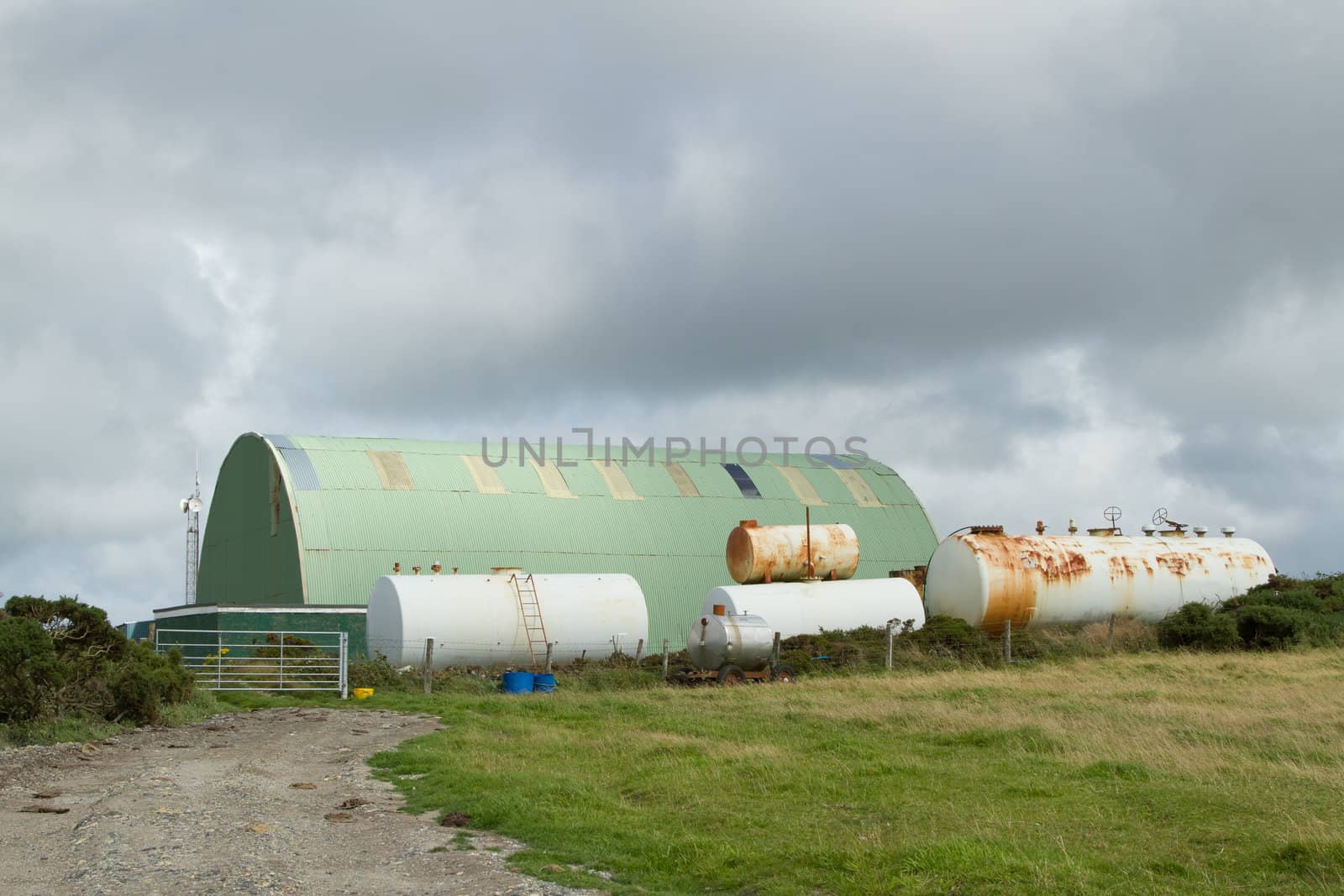 A track leads to a gate with white coloured chemical tanks and a green metal work shed.