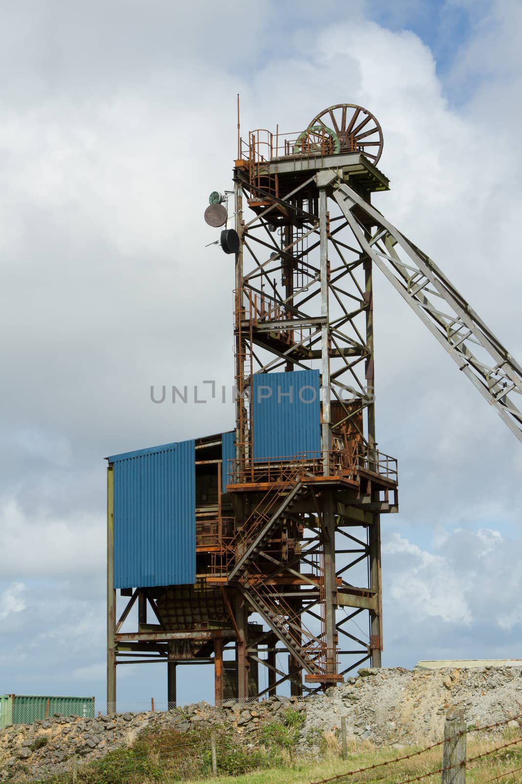 The tower structure of a minehead made of metal with supports and the winding wheel against a cloudy sky.