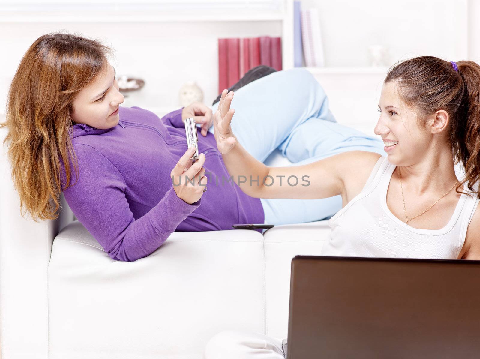 Two happy teenage girls having fun using electronic gadgets at home