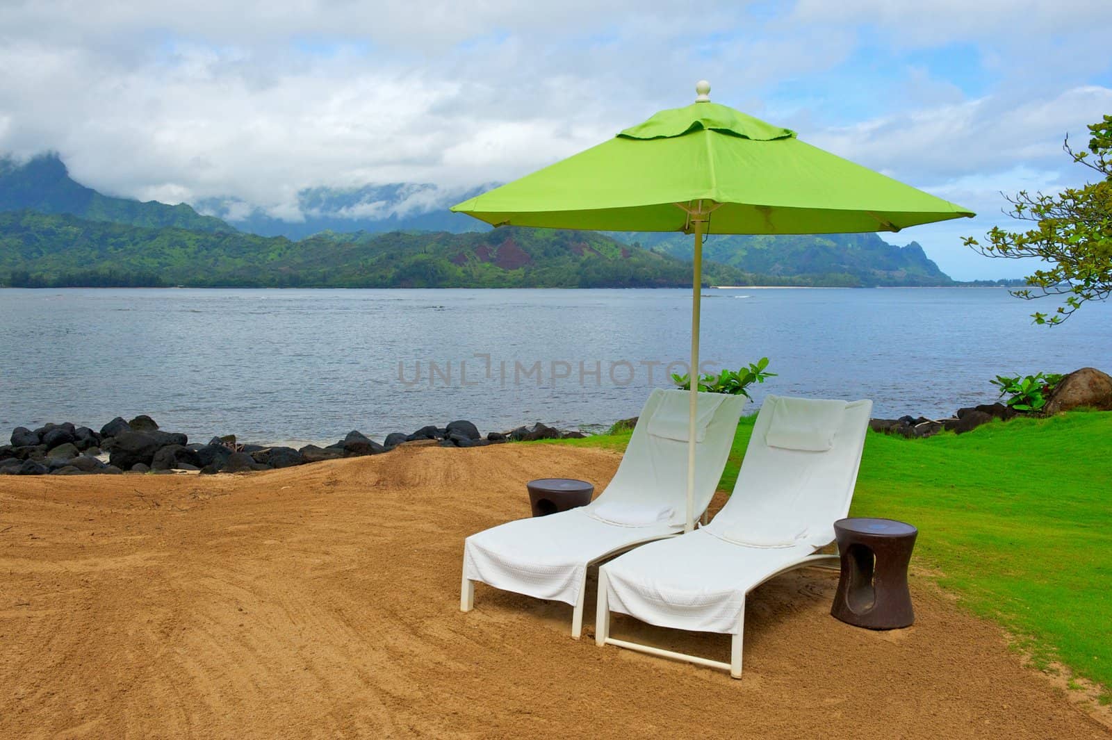 Two therapy chairs and a green ubmrella sit near the coastline on the island of Kauai in Hawaii