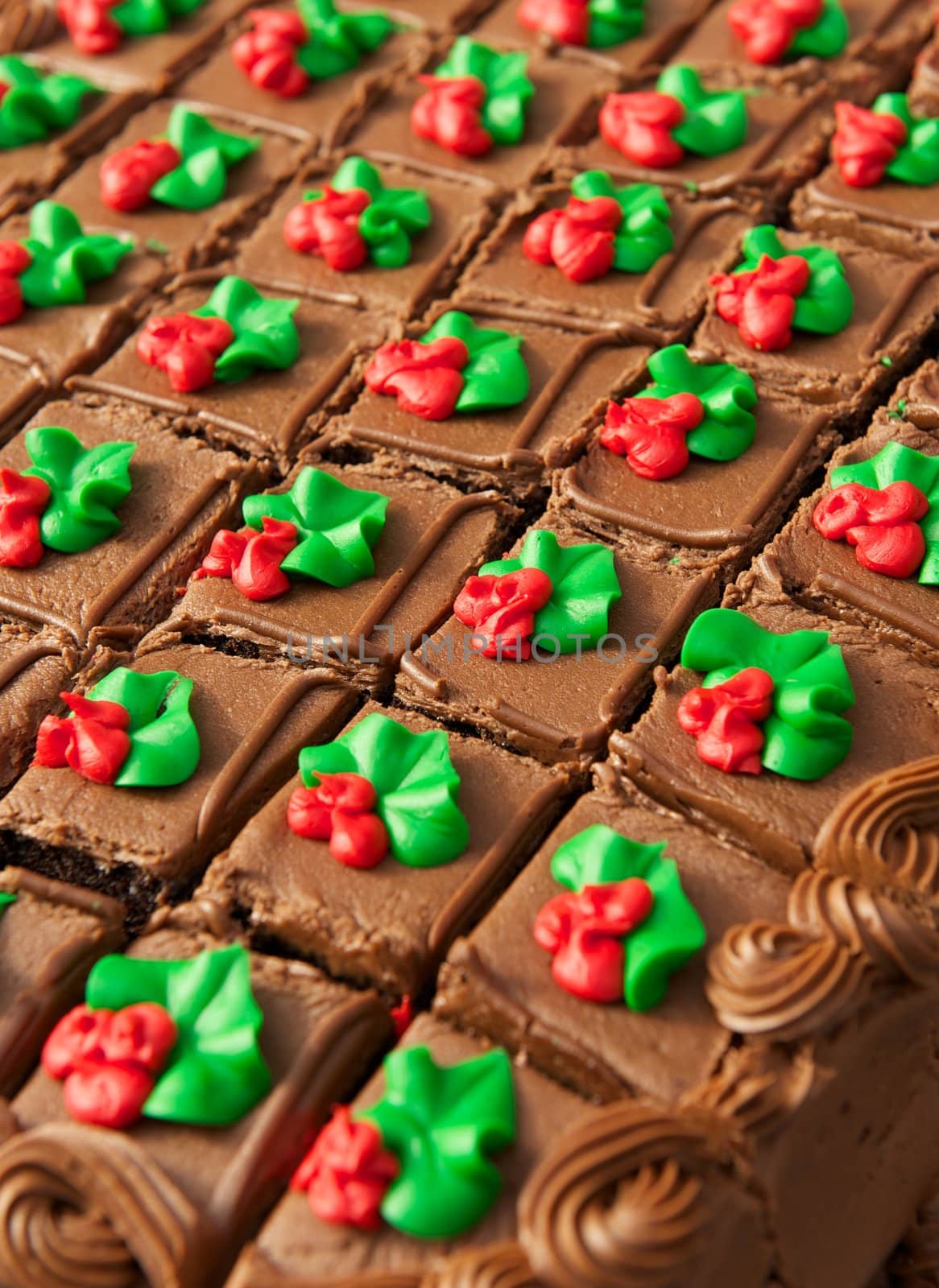A chocolate frosted cake cut into squares with a red flower and green leaf on each piece