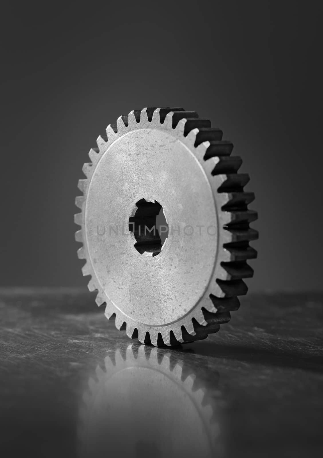 Black and white image of an old metallic cog gear on scratched metallic background. Short depth-of-field.