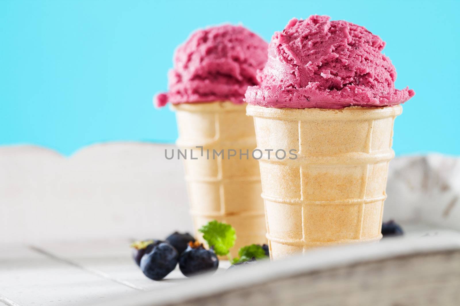blueberry ice cream in waffles behind white wood with blue background
