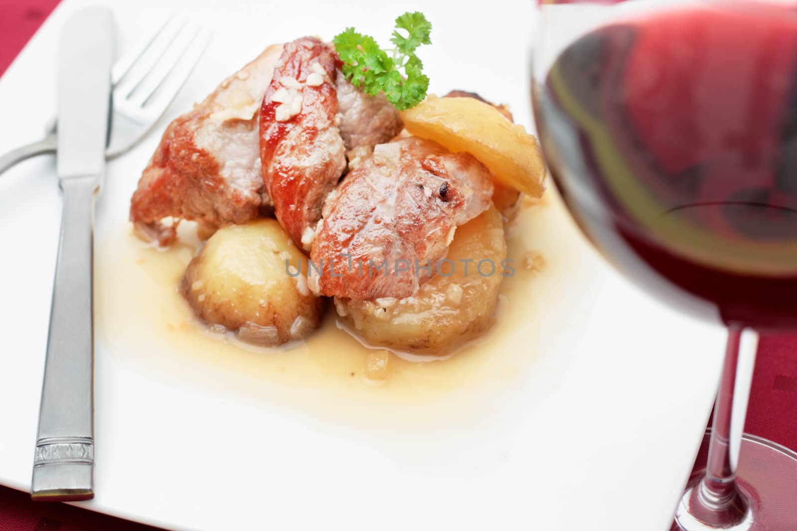 dish of pork sirloin steak stew with potatoes and onion sauce garlic and white wine with a glass of wine knife and fork