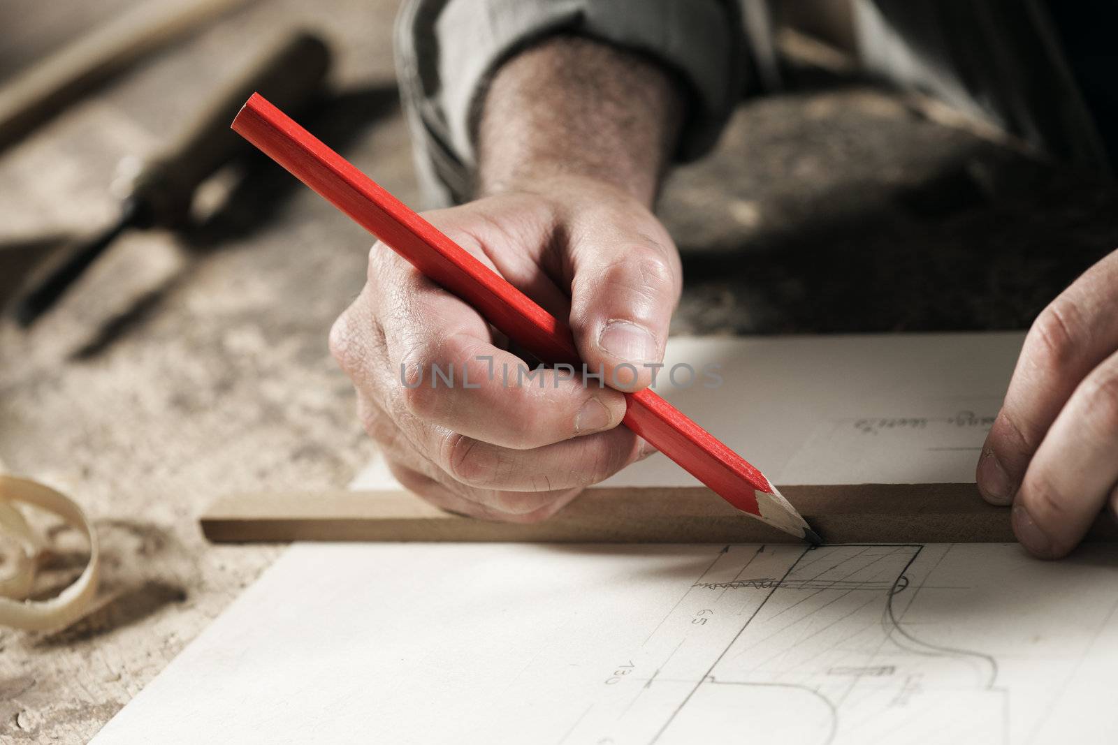 Closeup  view of a carpenter using a red pencil to draw a line on a blueprint