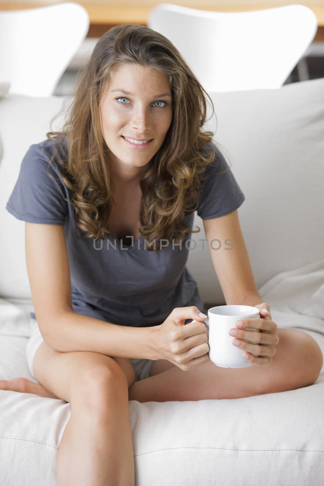 Portrait of a cute young lady sitting on sofa with a cup of coffee