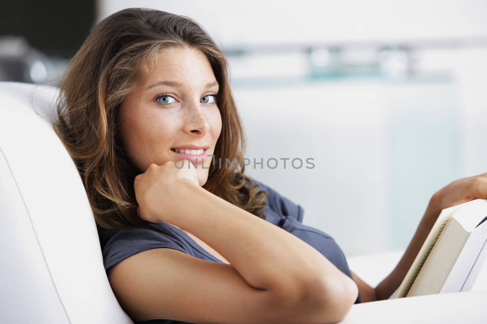 Young beautiful woman reading a book in a white armchair
