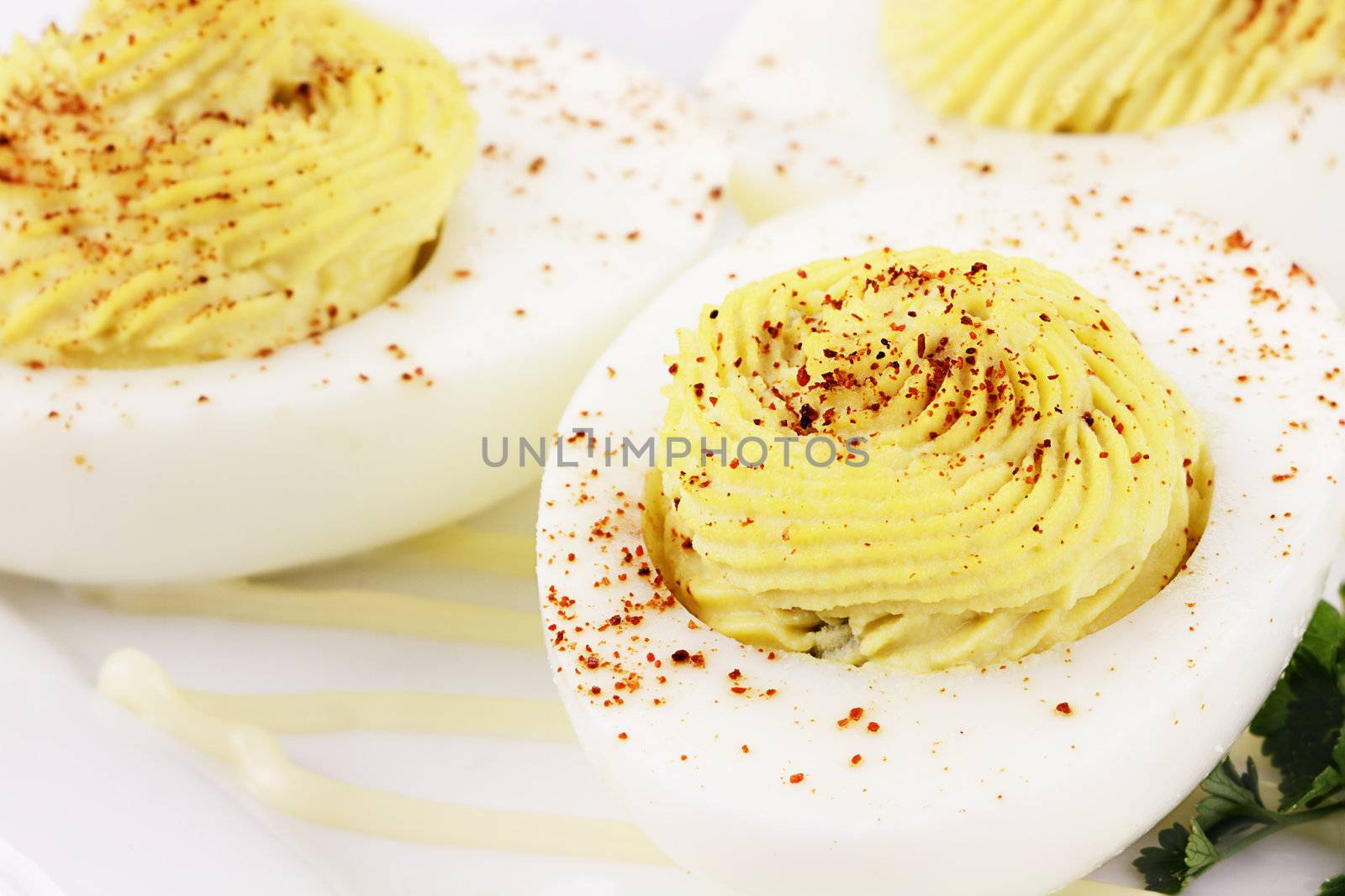 Plate of gourmet deviled eggs with a sprig of parsley over sauce. Extreme shallow depth of field with selective focus on egg in foreground.
