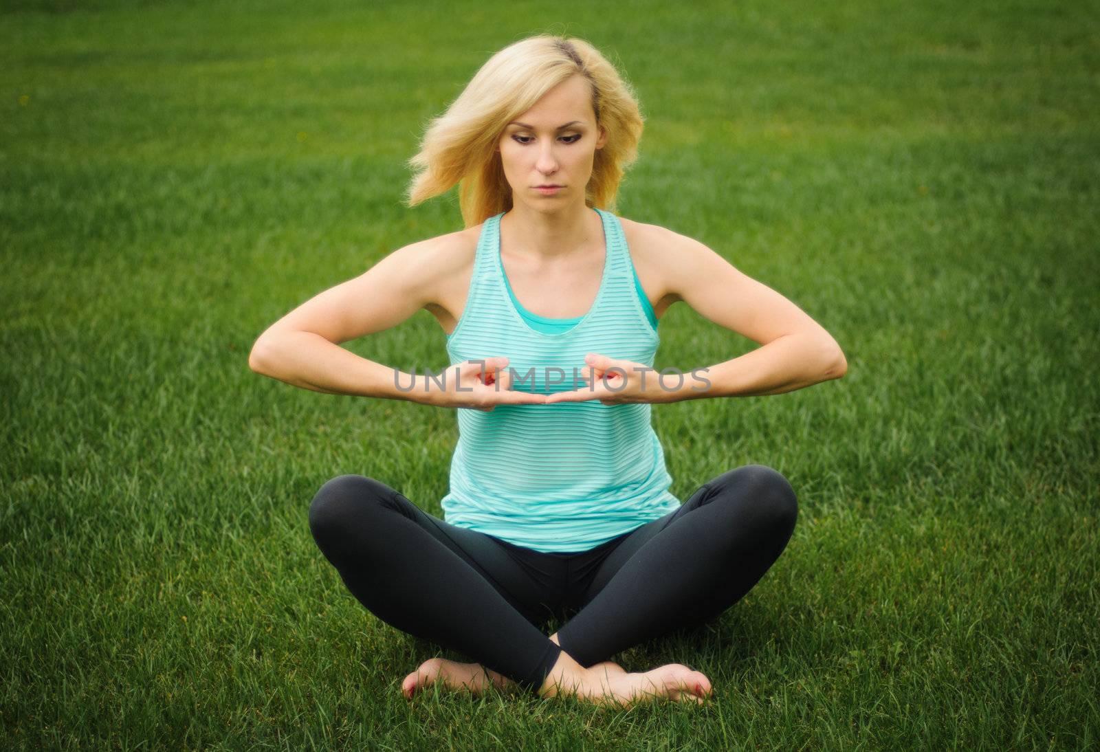 Blond woman on green grass doing yoga meditation